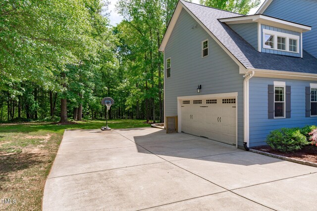view of side of home featuring an attached garage, driveway, and roof with shingles