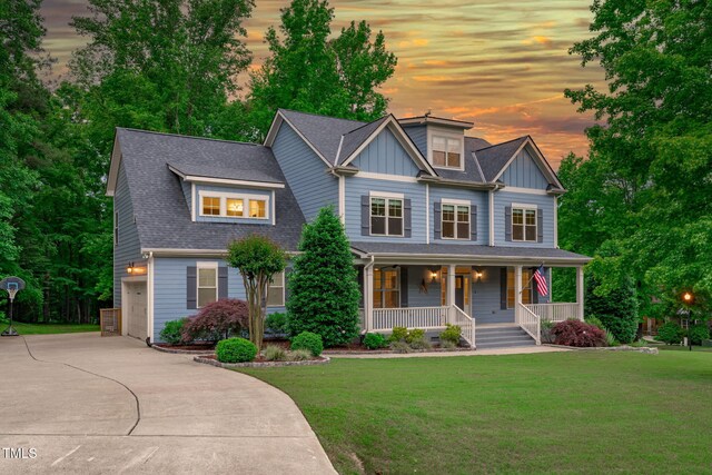 view of front facade with covered porch, concrete driveway, a front lawn, and board and batten siding