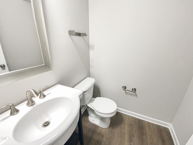 half bathroom with a sink, toilet, baseboards, and wood finished floors