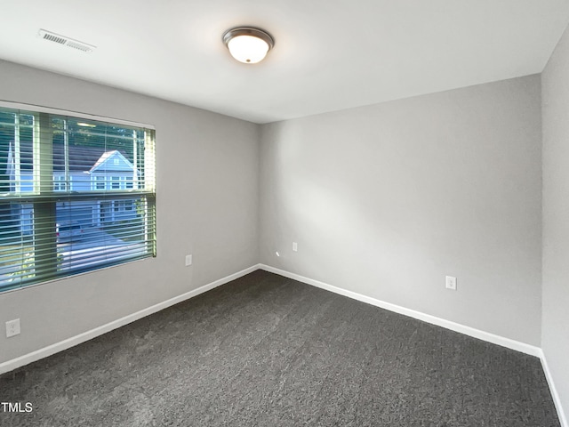 spare room featuring baseboards, dark carpet, and visible vents