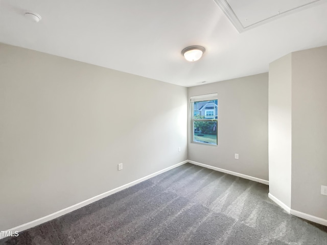 spare room featuring dark colored carpet, attic access, and baseboards