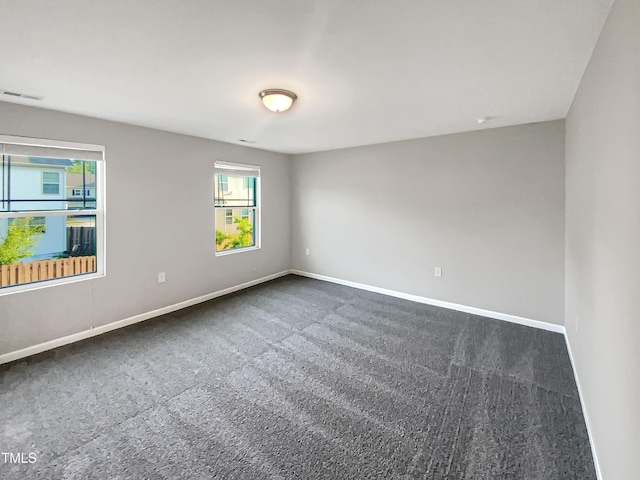 empty room featuring dark colored carpet, baseboards, and visible vents