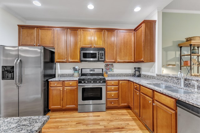 kitchen featuring stainless steel appliances, a sink, ornamental molding, light stone counters, and brown cabinetry