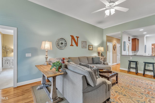 living area featuring light wood-style flooring, ceiling fan, baseboards, and ornamental molding