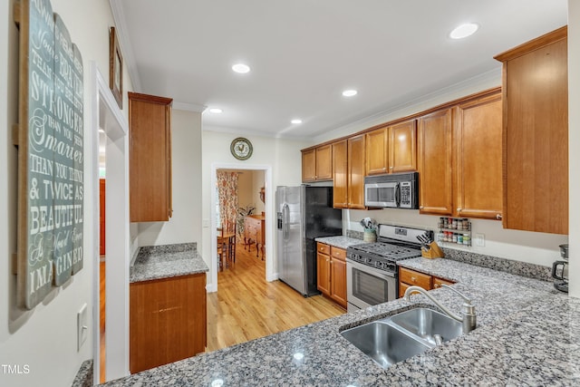 kitchen featuring appliances with stainless steel finishes, crown molding, a sink, light stone countertops, and brown cabinetry