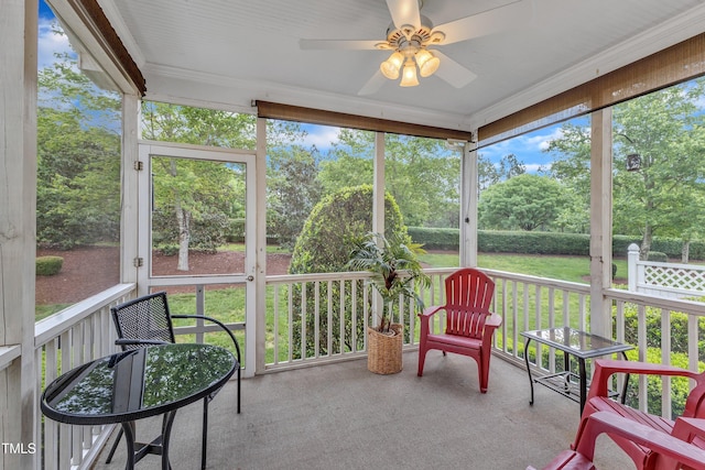 sunroom / solarium featuring ceiling fan, view of wooded area, and plenty of natural light