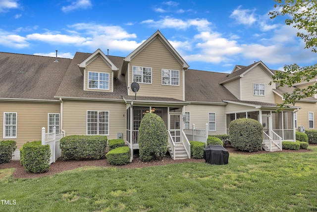 rear view of property featuring a sunroom, a yard, and roof with shingles