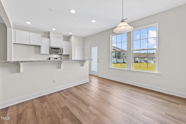 149 E Porthaven Way, Clayton, NC 27527 - kitchen with light wood-style flooring, a kitchen breakfast bar, white cabinets, stainless steel microwave, and light stone countertops