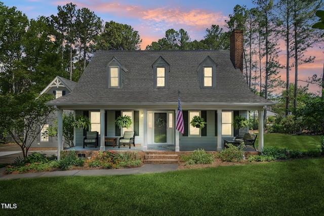 cape cod home with a porch, a lawn, a chimney, and roof with shingles