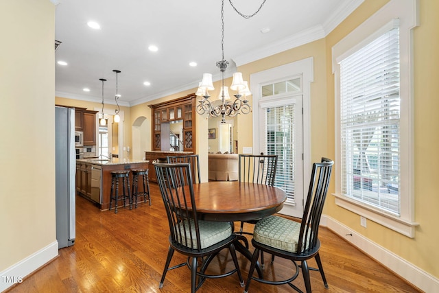 dining space featuring plenty of natural light, crown molding, baseboards, wood finished floors, and arched walkways