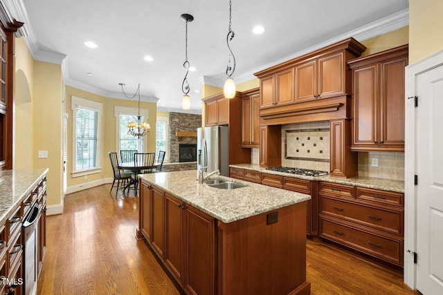 kitchen featuring appliances with stainless steel finishes, dark wood-style floors, tasteful backsplash, a center island with sink, and ornamental molding