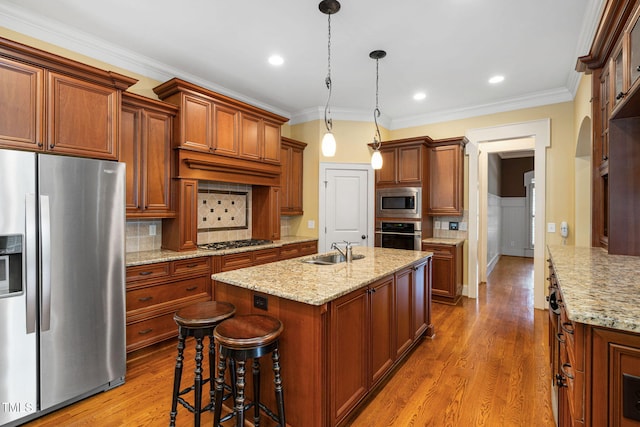 kitchen with stainless steel appliances, a sink, wood finished floors, a kitchen island with sink, and decorative backsplash
