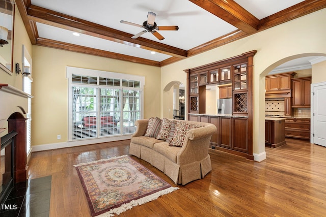 living area featuring arched walkways, a fireplace with flush hearth, ceiling fan, beam ceiling, and dark wood finished floors