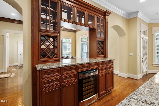 indoor dry bar featuring beverage cooler, arched walkways, wood finished floors, baseboards, and crown molding