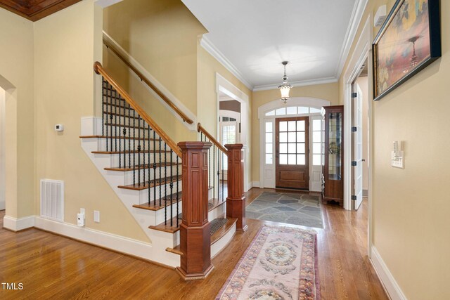 foyer with wood finished floors, baseboards, arched walkways, crown molding, and stairway