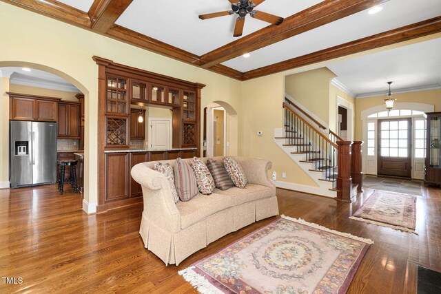 living room with arched walkways, a ceiling fan, dark wood-style flooring, stairway, and beamed ceiling