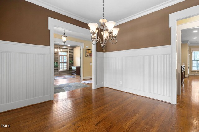 unfurnished dining area with a chandelier, wainscoting, crown molding, wood finished floors, and baseboards