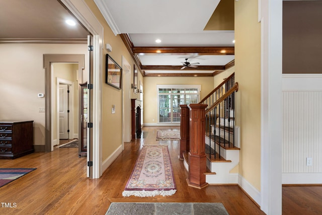 corridor featuring wood finished floors, ornamental molding, stairway, baseboards, and beamed ceiling