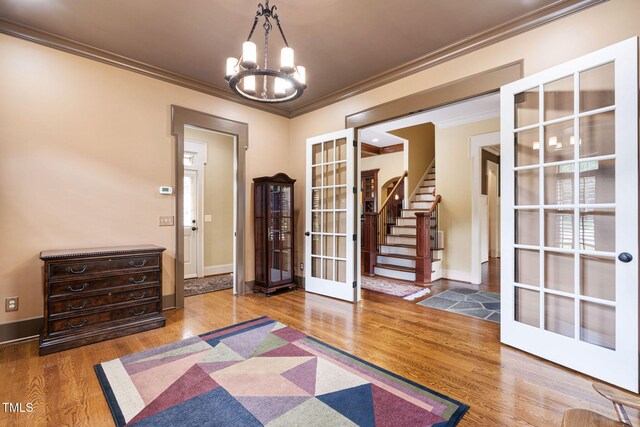foyer featuring french doors, crown molding, a chandelier, wood finished floors, and baseboards