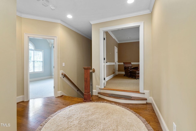 hallway with an upstairs landing, wood finished floors, ornamental molding, baseboards, and recessed lighting