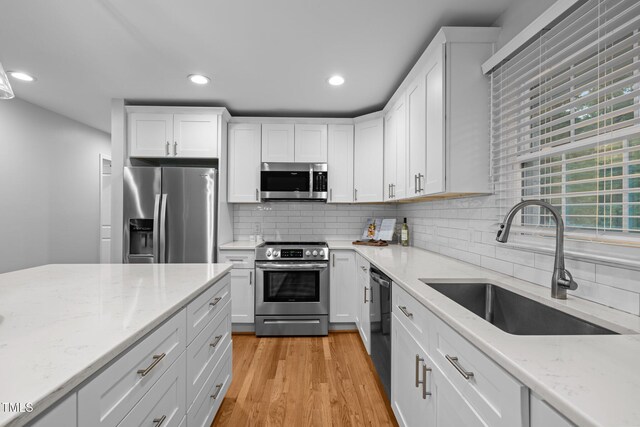 5208 Melbourne Rd, Raleigh, NC 27606 - kitchen with appliances with stainless steel finishes, a sink, white cabinets, decorative backsplash, and light wood finished floors