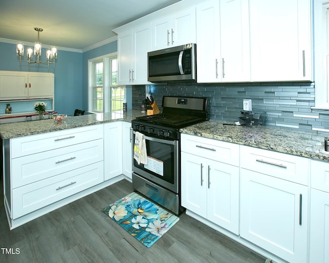 kitchen with appliances with stainless steel finishes, ornamental molding, a chandelier, a peninsula, and tasteful backsplash