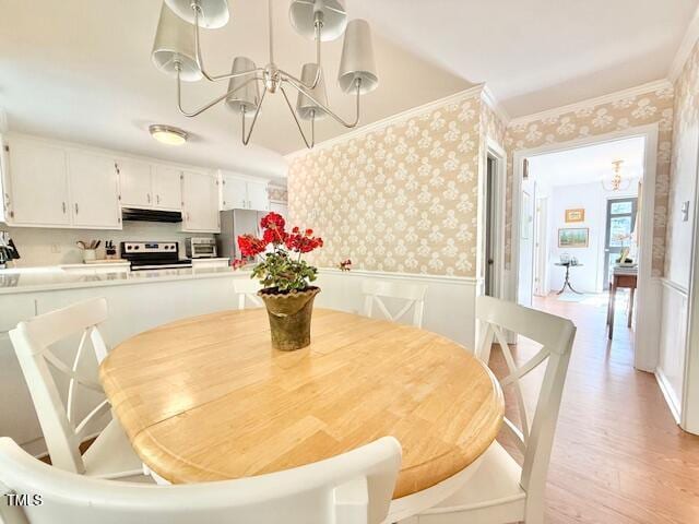 dining room featuring wallpapered walls, a chandelier, light wood-style flooring, ornamental molding, and a wainscoted wall