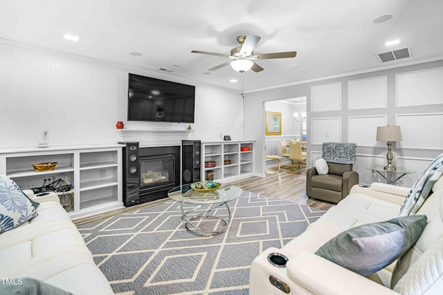 living room featuring ornamental molding, ceiling fan, wood finished floors, and a glass covered fireplace