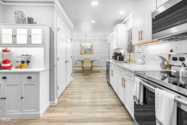 kitchen with appliances with stainless steel finishes, a sink, ornamental molding, light countertops, and light wood-style floors