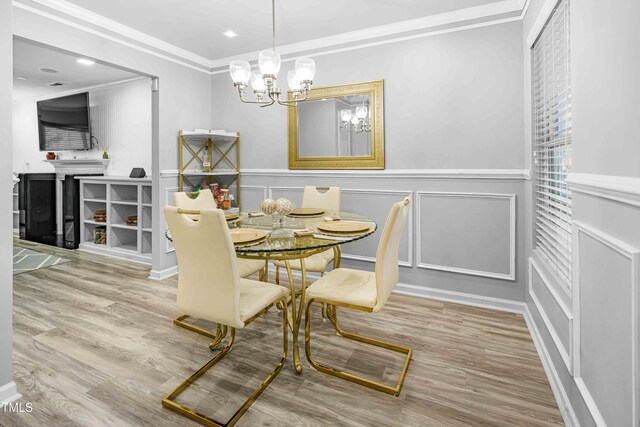 dining space with a decorative wall, crown molding, a chandelier, wood finished floors, and a wainscoted wall