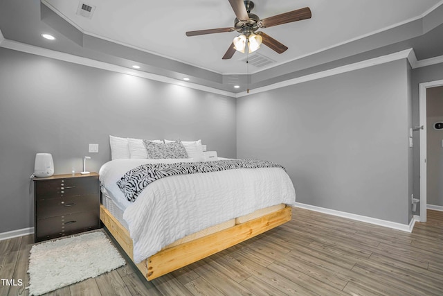 bedroom with a raised ceiling, ornamental molding, baseboards, wood finished floors, and recessed lighting