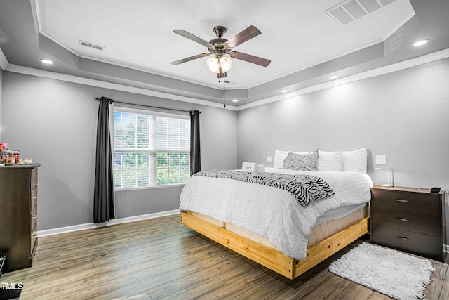 bedroom with a tray ceiling, ornamental molding, baseboards, wood finished floors, and recessed lighting