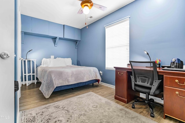 bedroom with a desk, multiple windows, wood finished floors, and baseboards