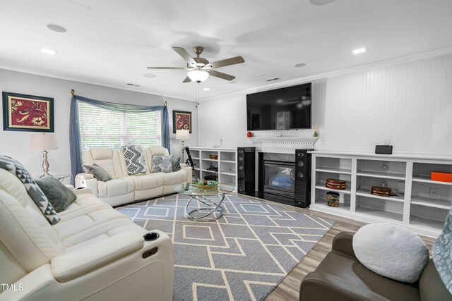 living area with ceiling fan, wood finished floors, ornamental molding, a fireplace with flush hearth, and recessed lighting