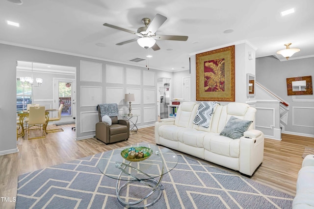 living area featuring a decorative wall, ornamental molding, a ceiling fan, light wood-style flooring, and stairs