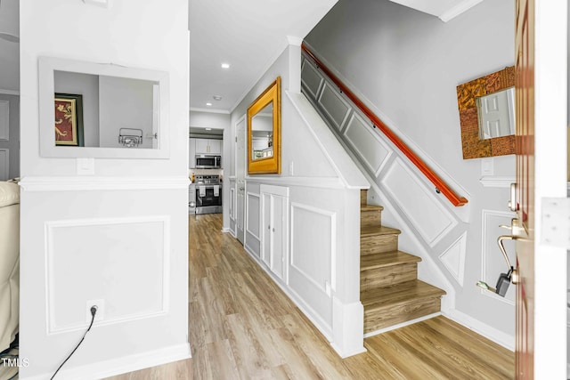 stairway featuring wood finished floors, a decorative wall, crown molding, and recessed lighting