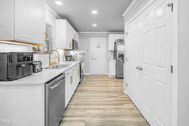 kitchen with stainless steel appliances, a sink, light wood finished floors, light countertops, and white cabinets