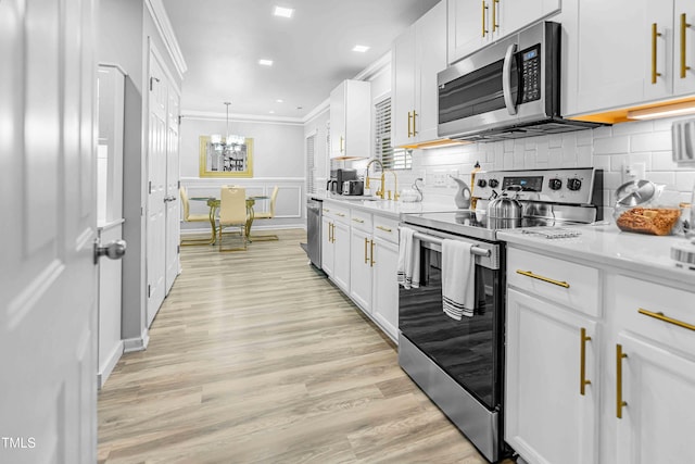 kitchen featuring stainless steel appliances, crown molding, light countertops, white cabinets, and a chandelier