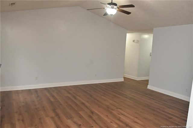spare room with ceiling fan, dark wood-type flooring, vaulted ceiling, and baseboards