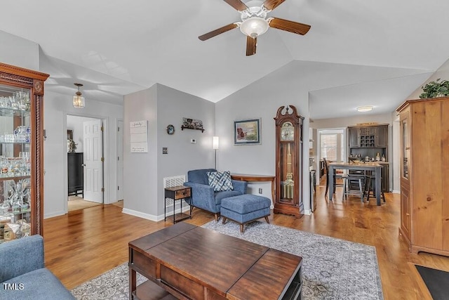 living area with a ceiling fan, vaulted ceiling, light wood-style flooring, and baseboards