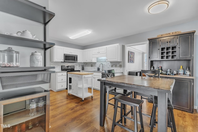 kitchen with appliances with stainless steel finishes, open shelves, backsplash, and white cabinets