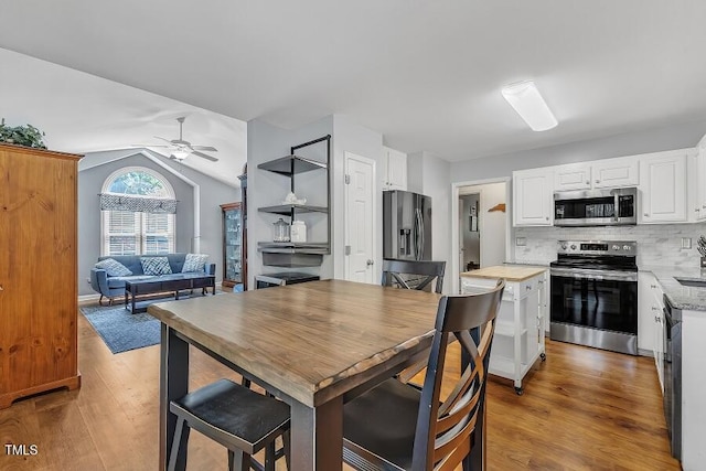 kitchen with stainless steel appliances, a ceiling fan, white cabinetry, wood finished floors, and vaulted ceiling
