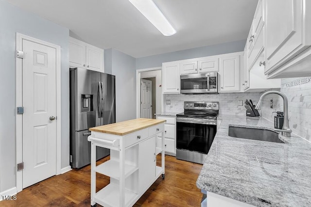 kitchen with appliances with stainless steel finishes, a sink, butcher block countertops, open shelves, and white cabinets