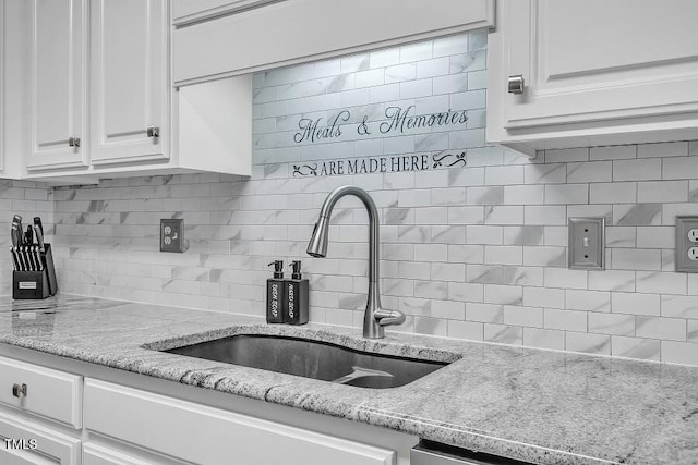 kitchen with a sink, decorative backsplash, white cabinets, and light stone countertops