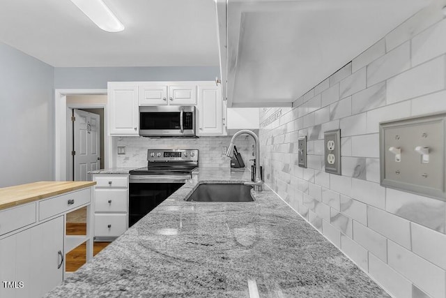 kitchen with appliances with stainless steel finishes, a sink, light stone counters, backsplash, and white cabinets