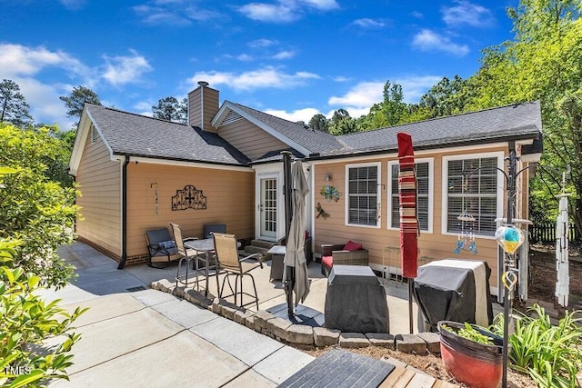 rear view of property with a patio, a chimney, and roof with shingles