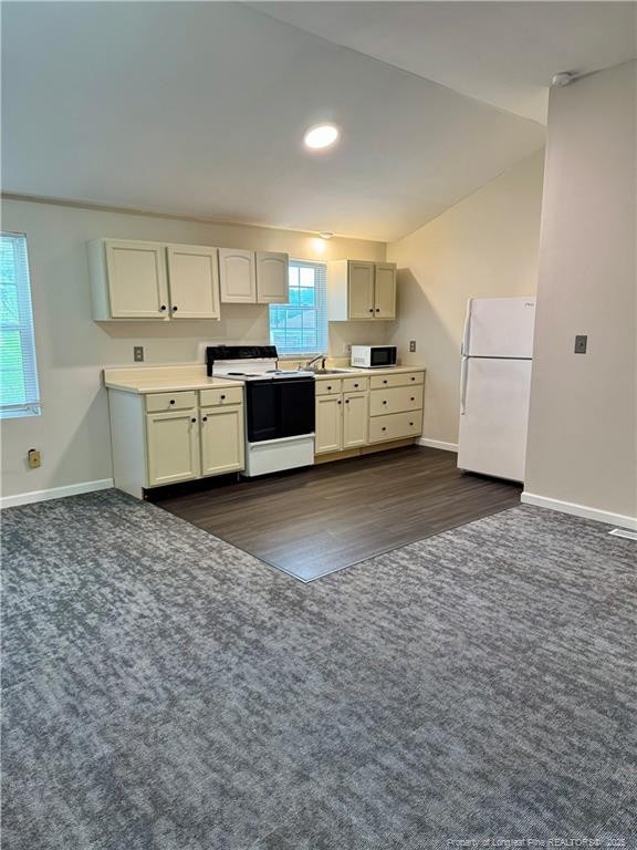 kitchen with a sink, dark carpet, dark wood-type flooring, baseboards, and white appliances