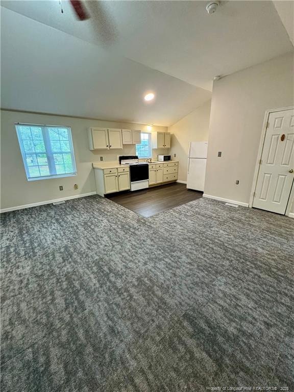 unfurnished living room featuring baseboards, a wealth of natural light, dark colored carpet, and vaulted ceiling