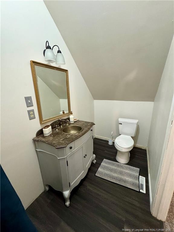 bathroom with lofted ceiling, toilet, wood finished floors, vanity, and visible vents