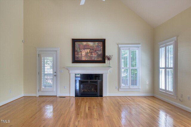 unfurnished living room with wood finished floors, plenty of natural light, high vaulted ceiling, and a fireplace with flush hearth